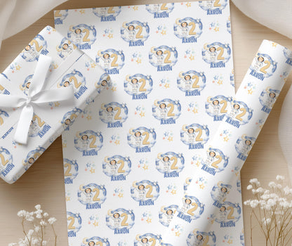 A pair of hands wrapping a gift box in the moon and stars space wrapping paper, finished with white ribbon