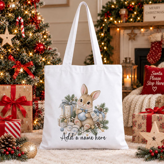 White cotton tote bag printed with a bunny rabbit in a blue striped scarf beside pale blue Christmas presents and baubles, with a personalised name below