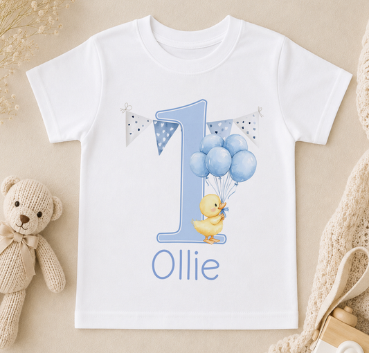 White t-shirt printed with a blue number 1, a yellow duck holding blue balloons and the personalised name 'Ollie'.