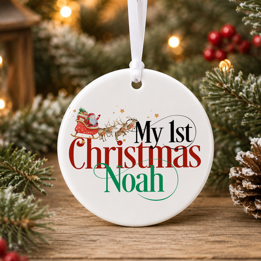 A white Christmas ornament with the text "My 1st Christmas Noah" printed on it, hanging on a Christmas tree with pine branches and red berries in the background.
