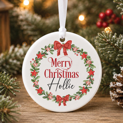 Personalised white ceramic Christmas bauble with a red berry and bow wreath framing “Merry Christmas” and a name