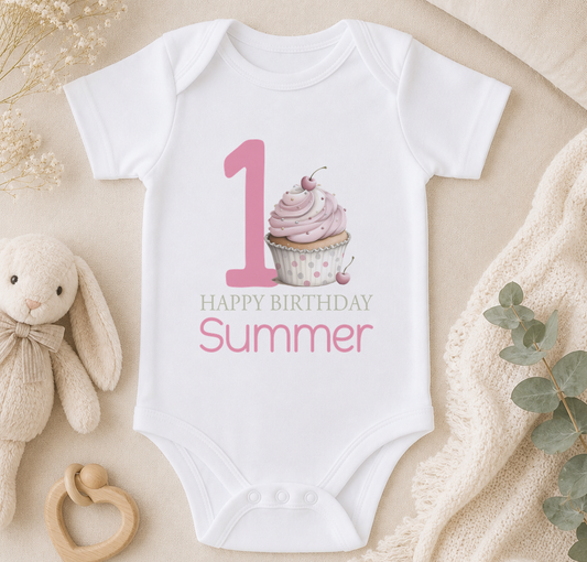 Personalised white baby vest printed with a pink cupcake, number one and 'Happy Birthday Summer', styled with a teddy bear