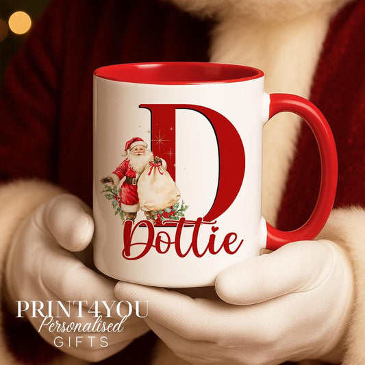 White ceramic mug with a red handle and rim, personalised with a large letter D featuring a Santa illustration and the name Dottie, held by a person in a Santa costume.