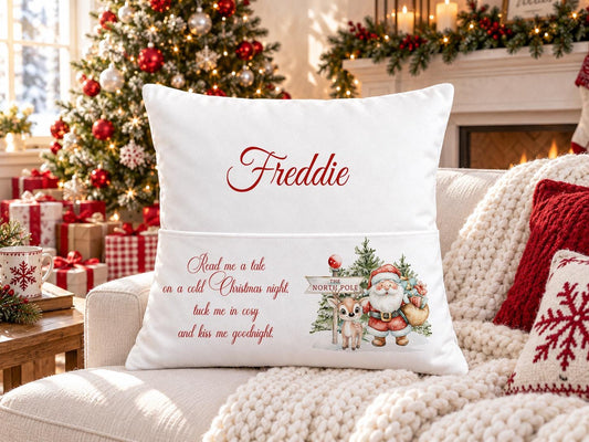 Personalised white Christmas book pocket cushion with Santa and a reindeer by a North Pole signpost, child’s name in red, on a festive sofa