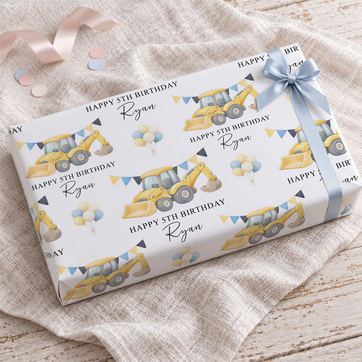 a gift box with a construction vehicle design and birthday decorations, including balloons and a ribbon.