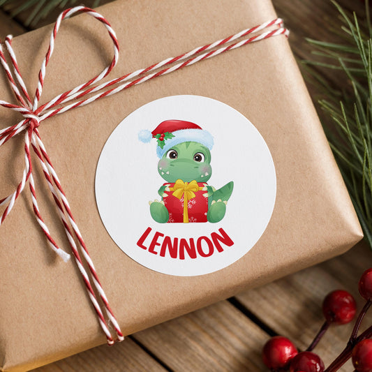 Personalised Santa dinosaur Christmas sticker with a child's name in bold red capitals, shown on a wrapped gift