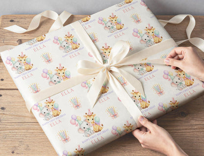 Gift wrapped in personalised giraffe and elephant first birthday paper, tied with cream ribbon on a wooden table