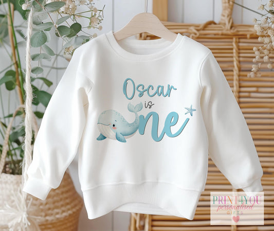 White baby sweatshirt in size 6-12 months personalised with a name and a hand-drawn whale ocean-theme first birthday design