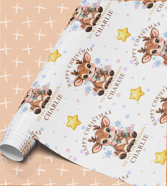 Personalised Christmas wrapping paper with a baby reindeer in a knitted scarf, gold stars and snowflakes, printed with Happy Christmas, To My Grandson and the name Charlie on a peach and white background