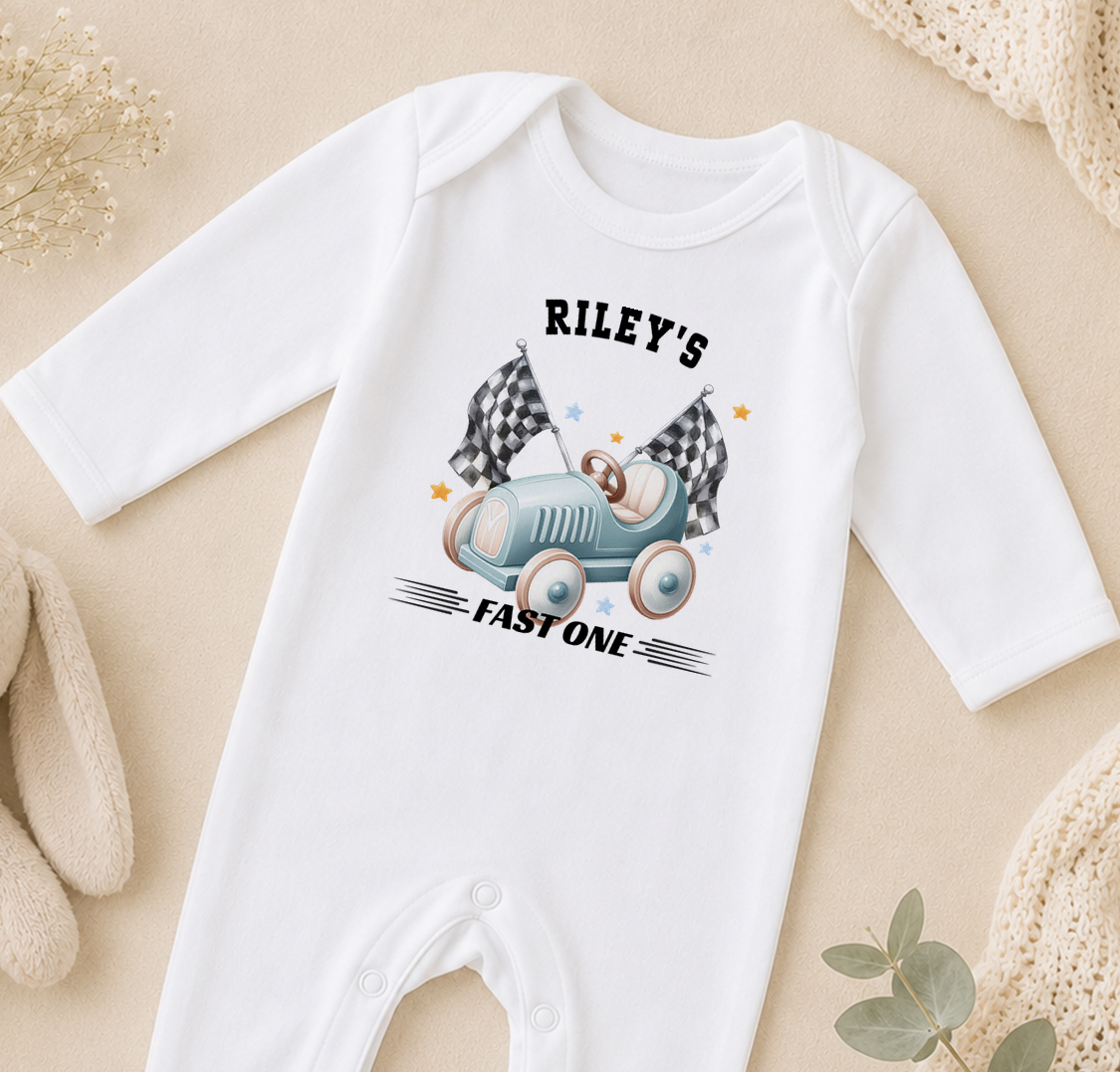 A white onesie with a graphic of a race car and the text "Riley's FAST ONE" printed on it.