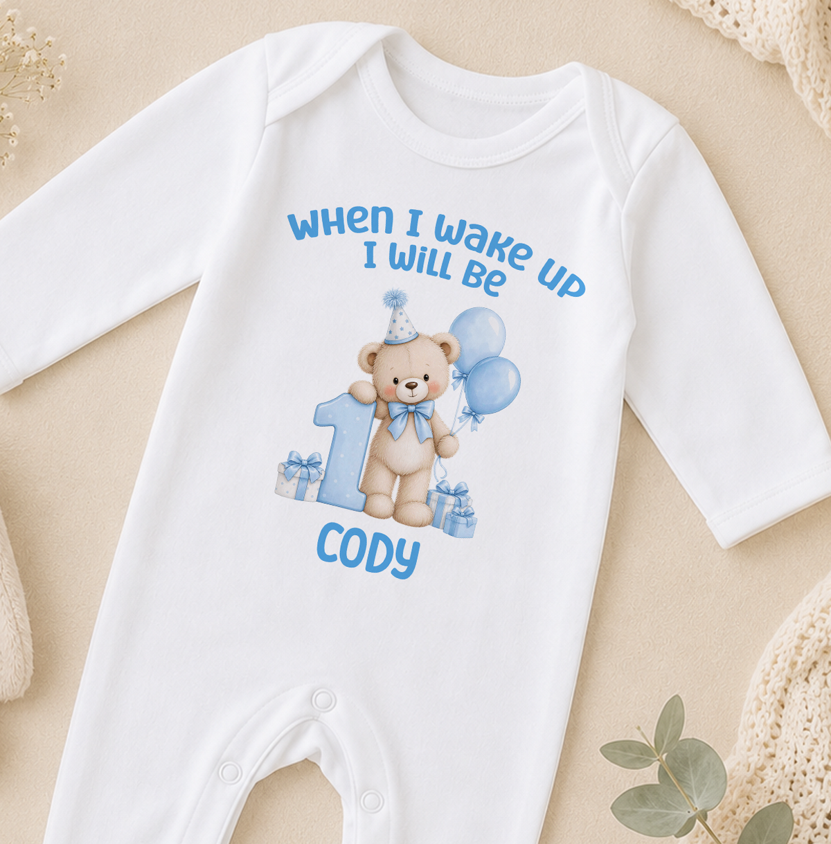 Personalised white baby sleepsuit printed When I Wake Up I Will Be 1 with a blue teddy bear, balloons and the name Cody