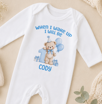 Personalised white baby sleepsuit printed When I Wake Up I Will Be 1 with a blue teddy bear, balloons and the name Cody