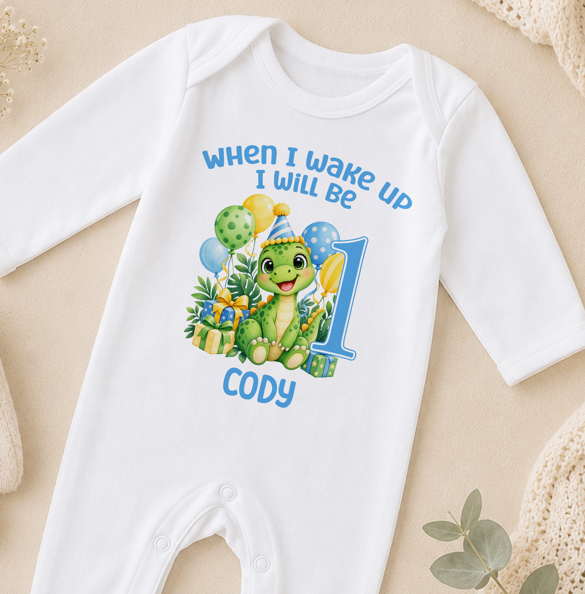 Personalised white baby sleepsuit printed When I Wake Up I Will Be 1 with a green dinosaur, balloons and the name Cody