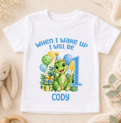 Personalised white baby t-shirt printed When I Wake Up I Will Be 1 with a green dinosaur, balloons and the name Cody