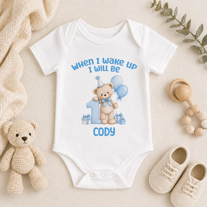 Personalised white baby vest printed When I Wake Up I Will Be 1 with a blue teddy bear, balloons and the name Cody