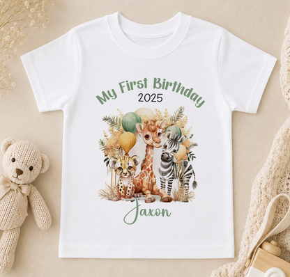A white t-shirt with a printed design of a giraffe, zebra, and other animals, along with the text "My First Birthday 2025" and "Jaxon".