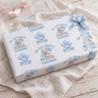 a gift box with a teddy bear and balloons printed on it, along with the text "Mr. One-Derrful" and "Freddie" printed on it.