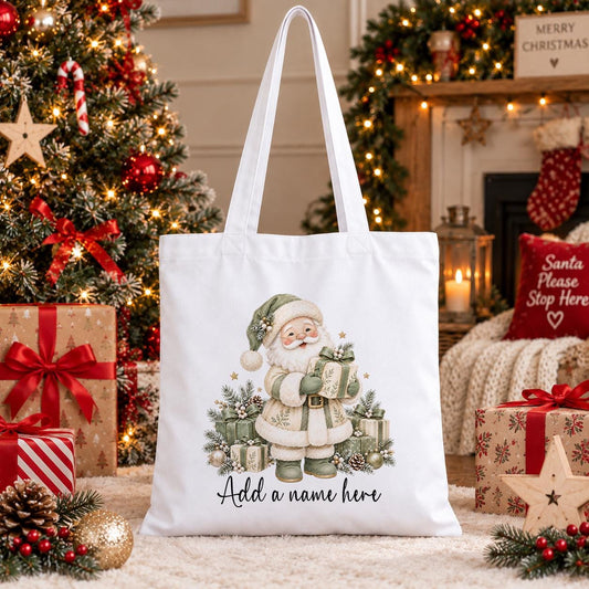 White cotton tote bag printed with a watercolour Father Christmas in a sage green coat holding presents, above a personalised name