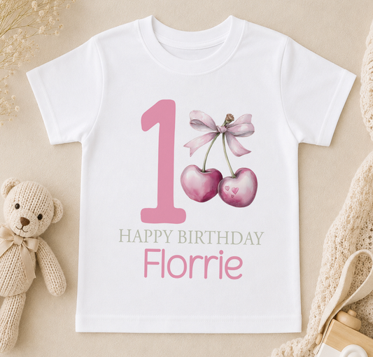 Personalised t-shirt printed with a pink number one, cherry and bow design, and 'Happy Birthday Florrie' lettering