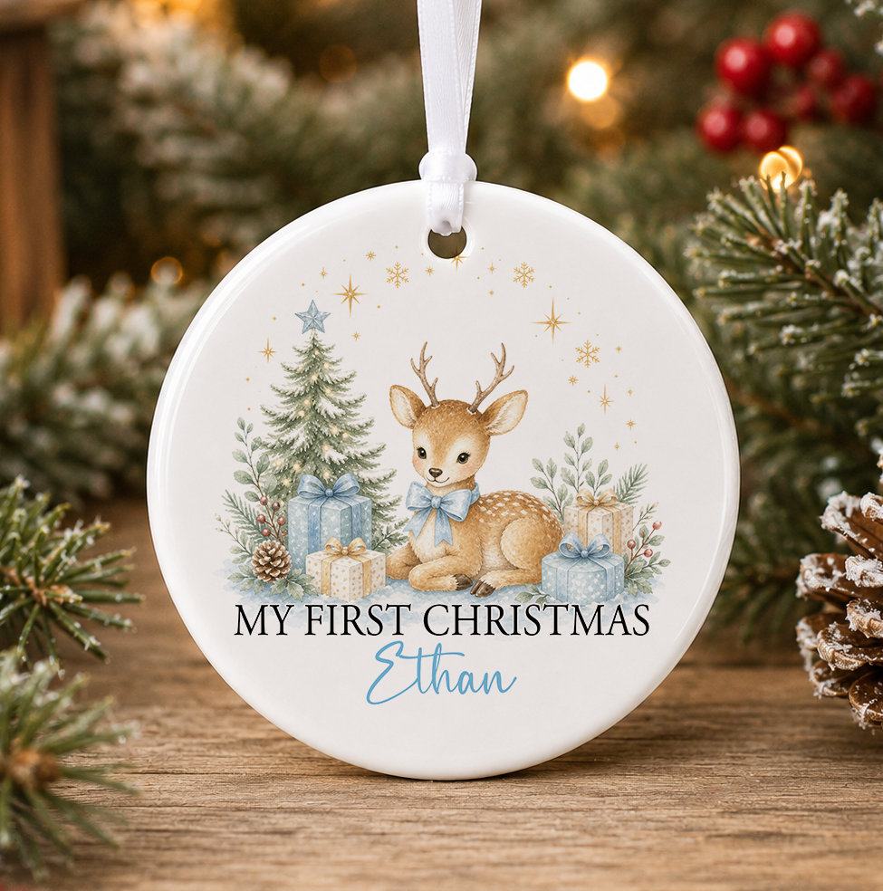 Personalised blue reindeer My First Christmas bauble, white ceramic ornament with a baby reindeer wearing a blue bow beside a Christmas tree with blue and gold presents, printed with a baby's name in blue script