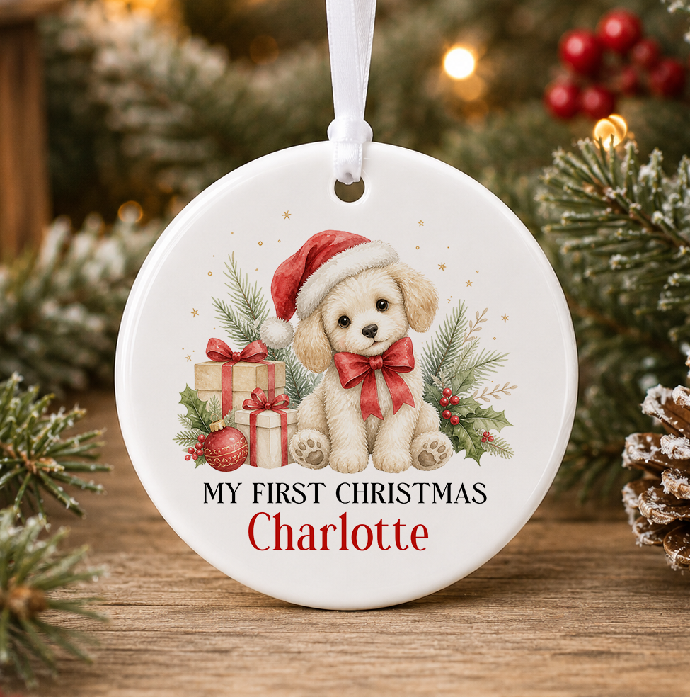 Personalised puppy My First Christmas bauble, white ceramic ornament with a fluffy cream puppy in a Santa hat and red bow beside presents and holly, printed with a baby's name in red