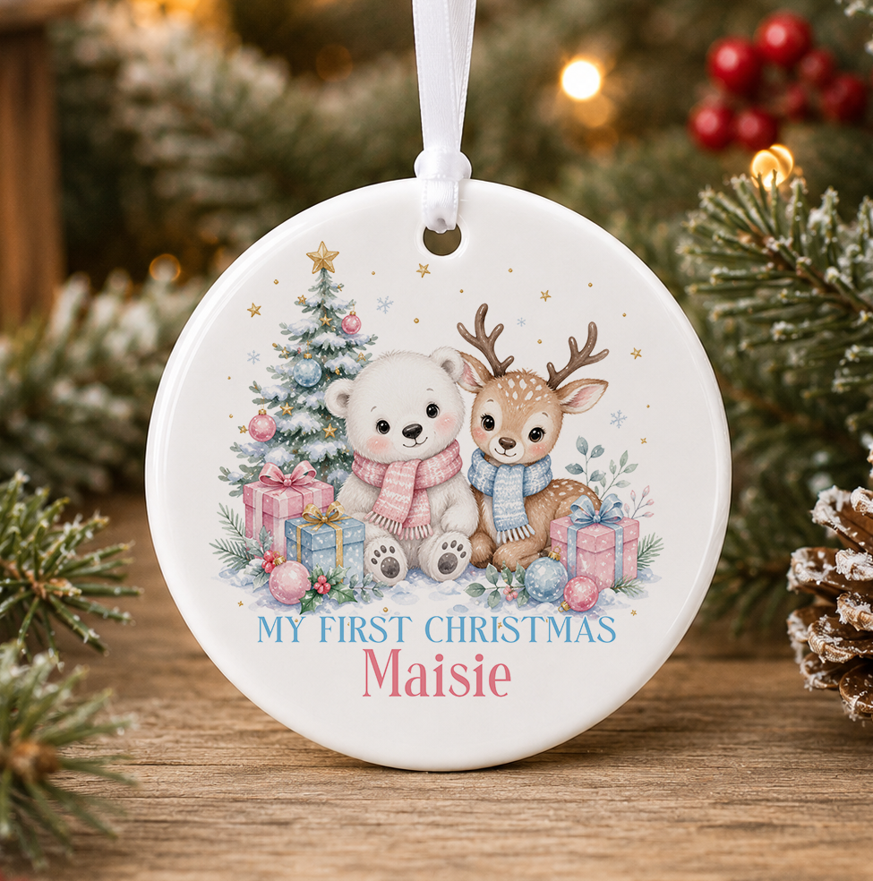 Personalised polar bear and reindeer My First Christmas bauble, white ceramic ornament with a polar bear in a pink scarf and reindeer in a blue scarf beside a Christmas tree and presents, printed with a baby's name