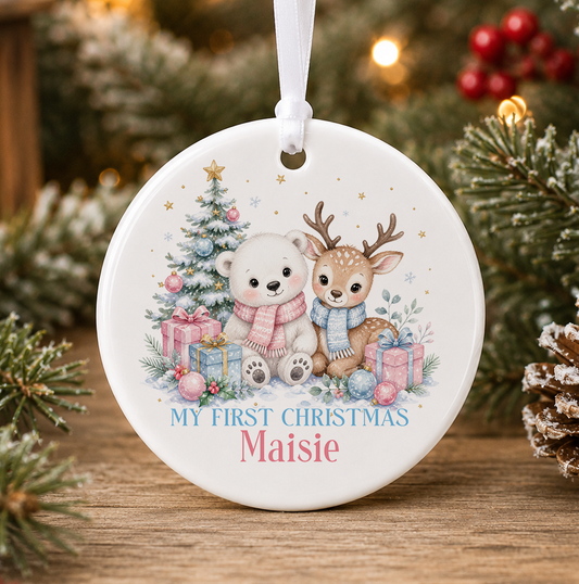 Personalised polar bear and reindeer My First Christmas bauble, white ceramic ornament with a polar bear in a pink scarf and reindeer in a blue scarf beside a Christmas tree and presents, printed with a baby's name