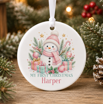 Personalised pink snowman My First Christmas bauble, white ceramic ornament with a snowman in a pink bobble hat and scarf, pink and mint presents and gold stars, printed with a baby's name
