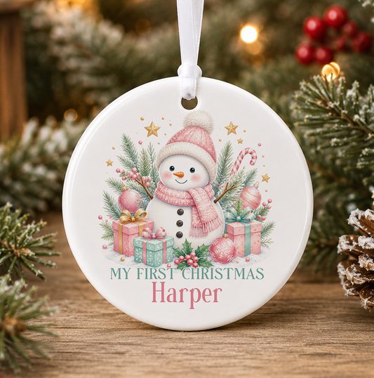 Personalised pink snowman My First Christmas bauble, white ceramic ornament with a snowman in a pink bobble hat and scarf, pink and mint presents and gold stars, printed with a baby's name