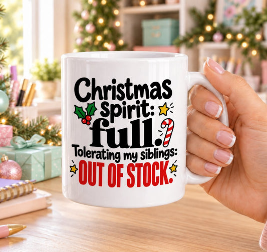 White 11oz ceramic Christmas mug printed with “Christmas spirit: full. Tolerating my siblings: out of stock.” in black and red lettering with holly and a candy cane, held in a festive room