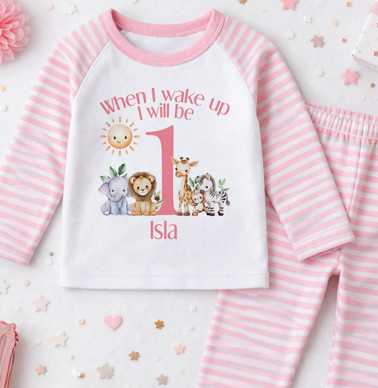 A pink and white striped onesie with a printed design of a baby elephant, giraffe, lion, and zebra, along with the text "When I wake up I will be 1" and the name "Isla".