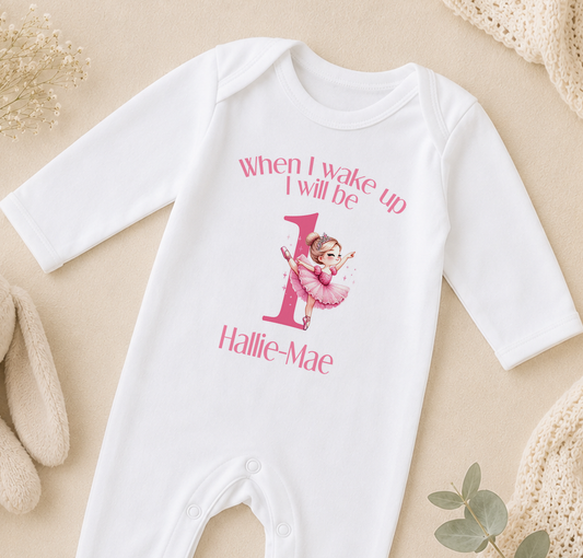 A white onesie with a pink cartoon character and text printed on it, placed on a beige surface.