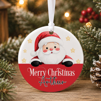 Personalised white ceramic Christmas bauble with Santa peeking over a red band, “Merry Christmas” and a name, hanging on a tree