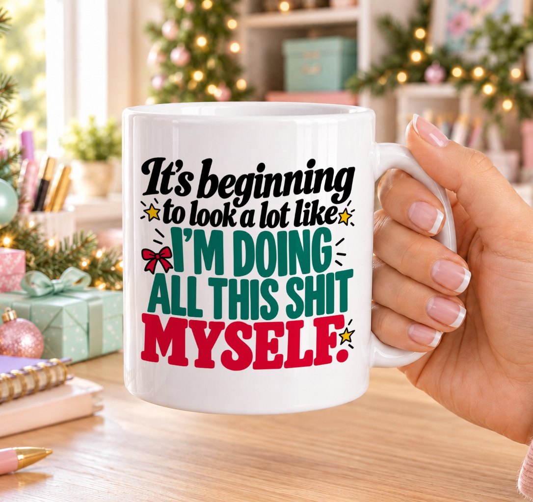 White 11oz ceramic Christmas mug printed with “It’s beginning to look a lot like I’m doing all this shit myself.” in red, green and black lettering with a red bow and gold stars, held in a festive room