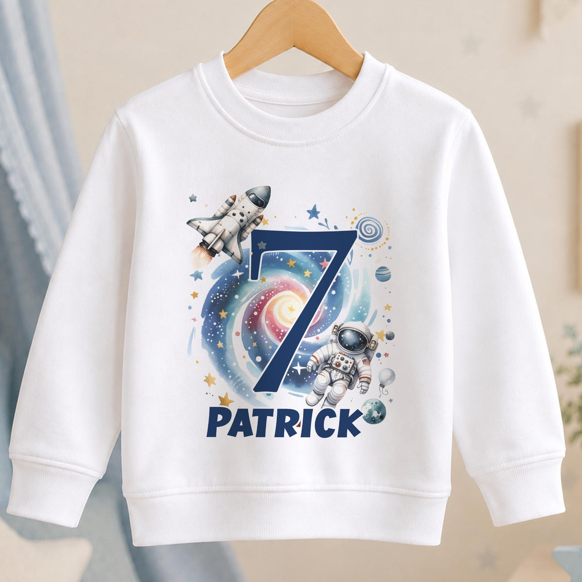 Personalised space birthday sweatshirt – white sweatshirt with a navy number 7 over a galaxy with a rocket and astronaut, and the name Patrick