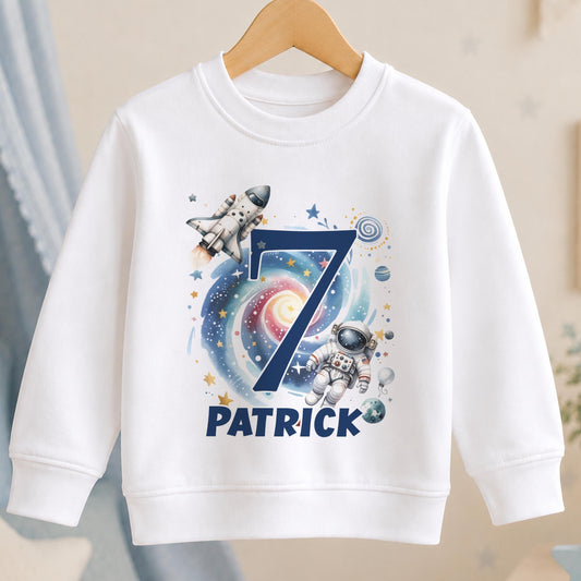 Personalised space birthday sweatshirt – white sweatshirt with a navy number 7 over a galaxy with a rocket and astronaut, and the name Patrick
