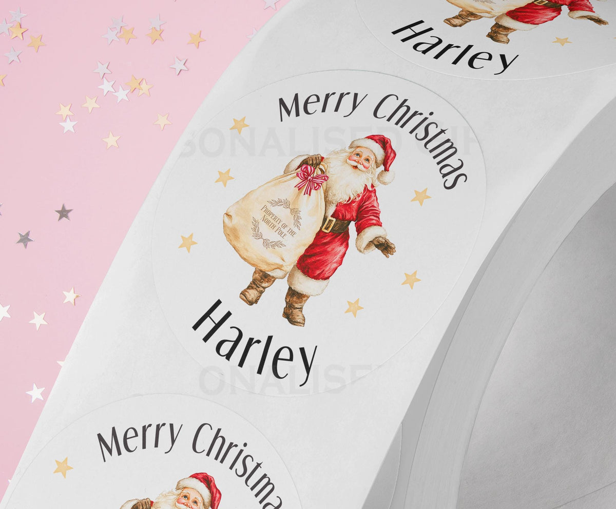 Personalised festive Santa Christmas sticker with a custom name printed alongside, glossy white round gift label on a strip