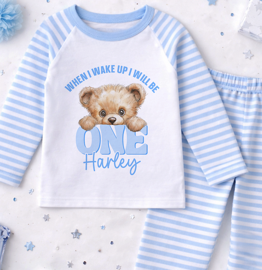 A white and blue striped pajama set with a teddy bear graphic and text, along with some confetti on the floor.