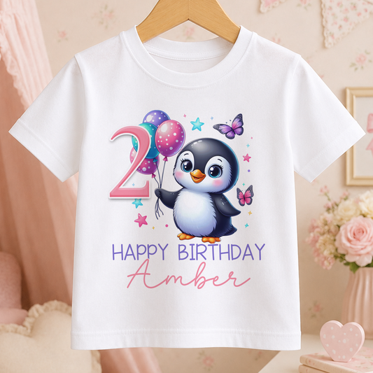 A white t-shirt with a cartoon penguin and balloons, along with the text "Happy Birthday Amber" printed on it.