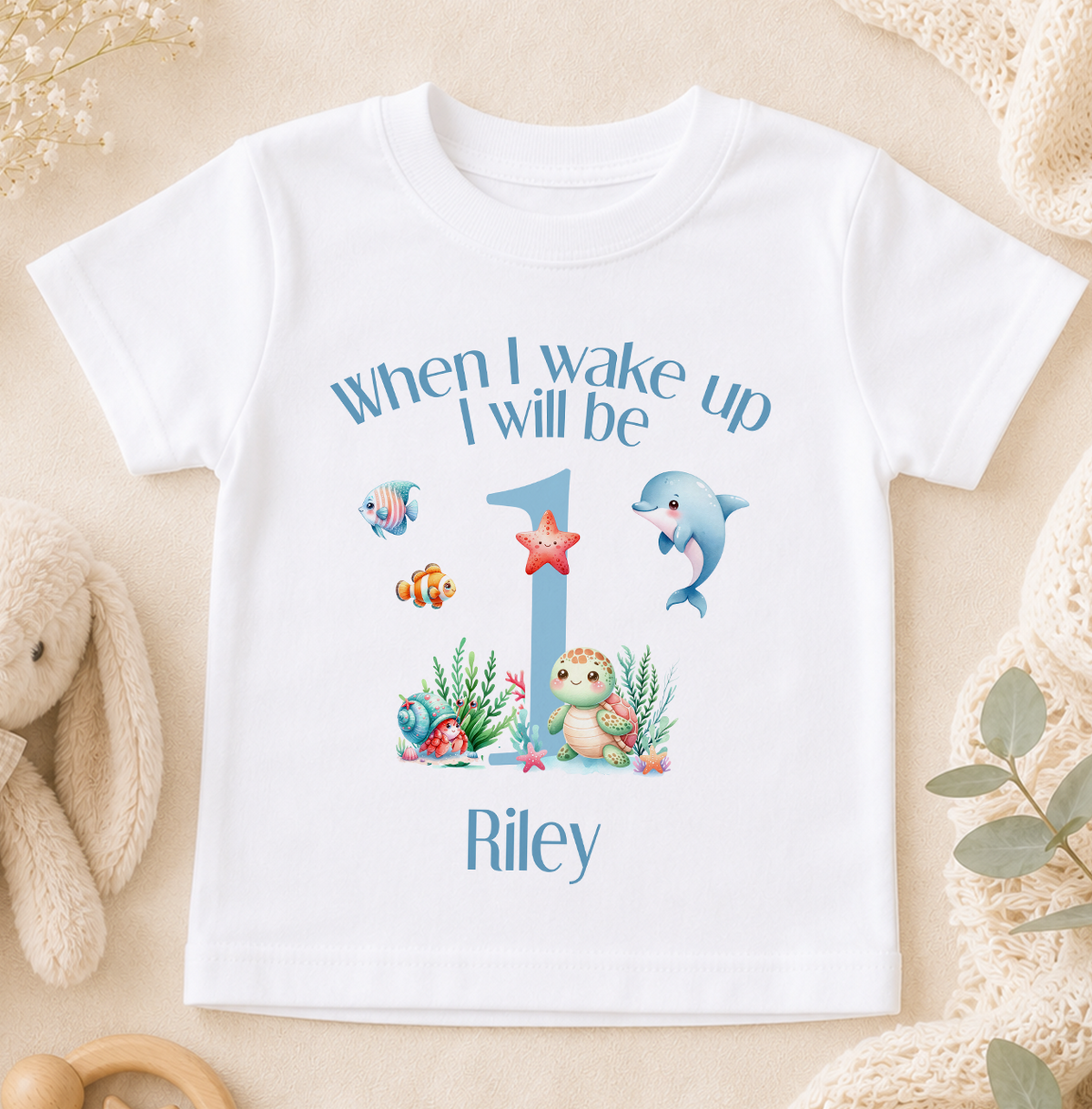 A white t-shirt with a personalized design featuring a cartoon character and the text "When I wake up I will be 1 Riley".
