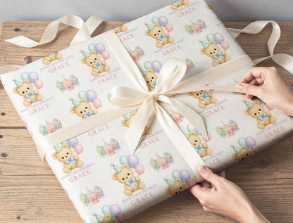 Gift wrapped in personalised first birthday teddy bear and cupcake wrapping paper, tied with a cream ribbon on a wooden table