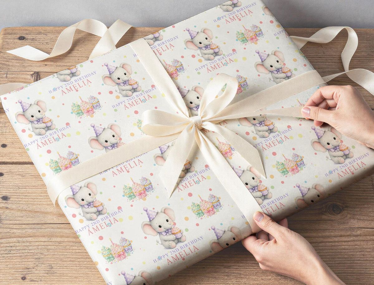 Gift wrapped in personalised elephant and cupcake birthday paper, tied with cream ribbon on a wooden table