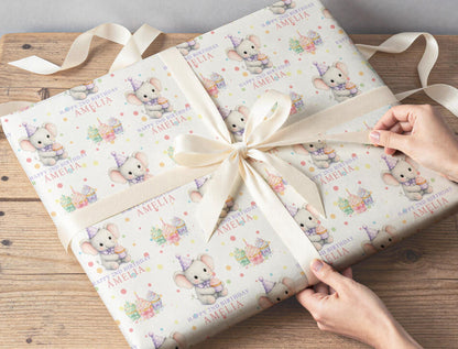 Gift wrapped in personalised elephant and cupcake birthday paper, tied with cream ribbon on a wooden table
