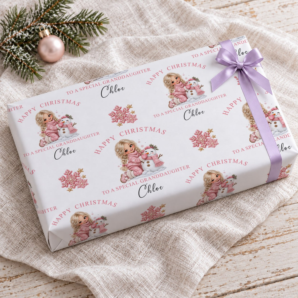 Gift wrapped in personalised girl and snowman Christmas wrapping paper with a lilac bow on a linen cloth