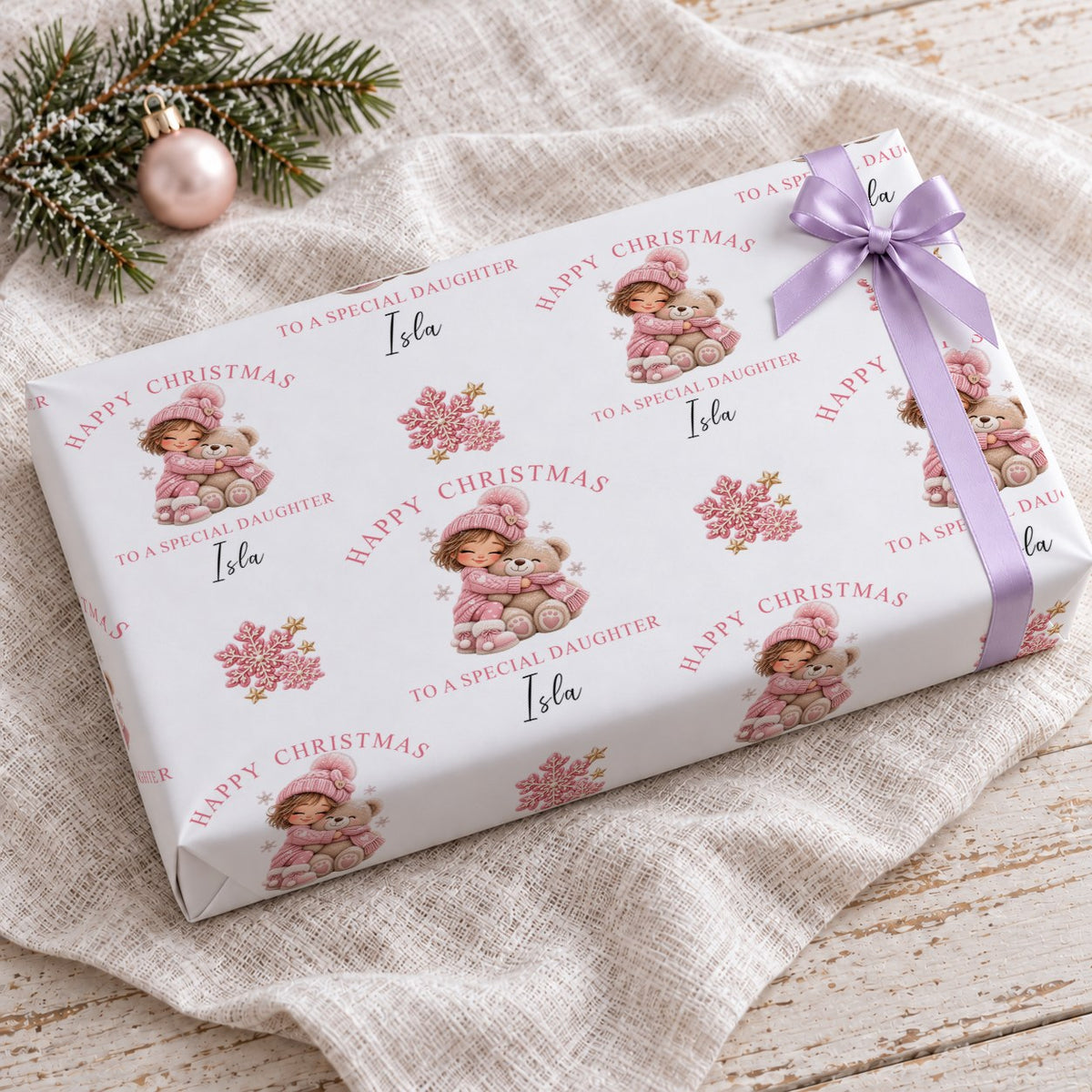 Gift wrapped in personalised girl and teddy bear Christmas wrapping paper with a lilac bow on a linen cloth
