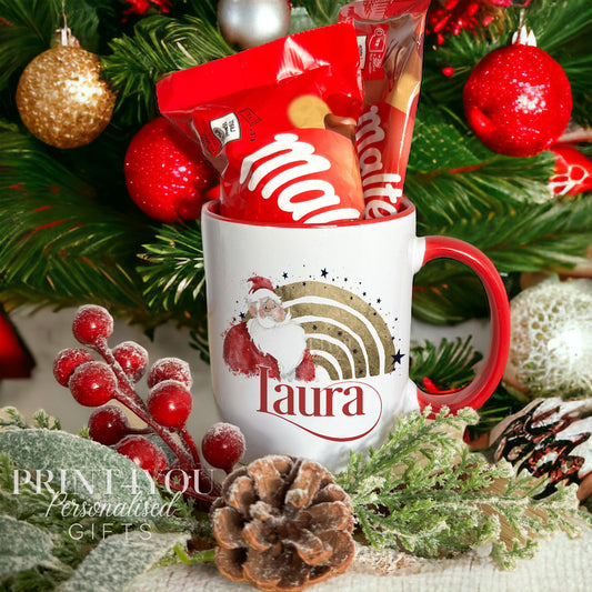 White ceramic Christmas mug with a red handle, personalised with a custom name and a gold foil rainbow Santa design