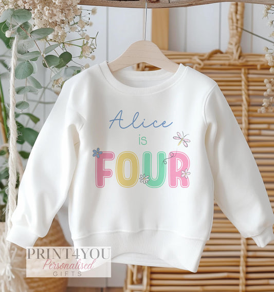 White children's cotton sweatshirt jumper with a personalised name and pastel daisy birthday number design, laid flat, front view