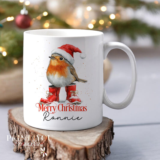 White ceramic mug personalised with 'Merry Christmas' and a custom name, featuring a festive robin wearing a Santa hat