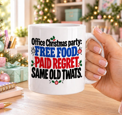 White 11oz ceramic Christmas mug printed with “Office Christmas party: Free food. Paid regret. Same old twats.” in red, green and black lettering with baubles and holly, held in a festive room