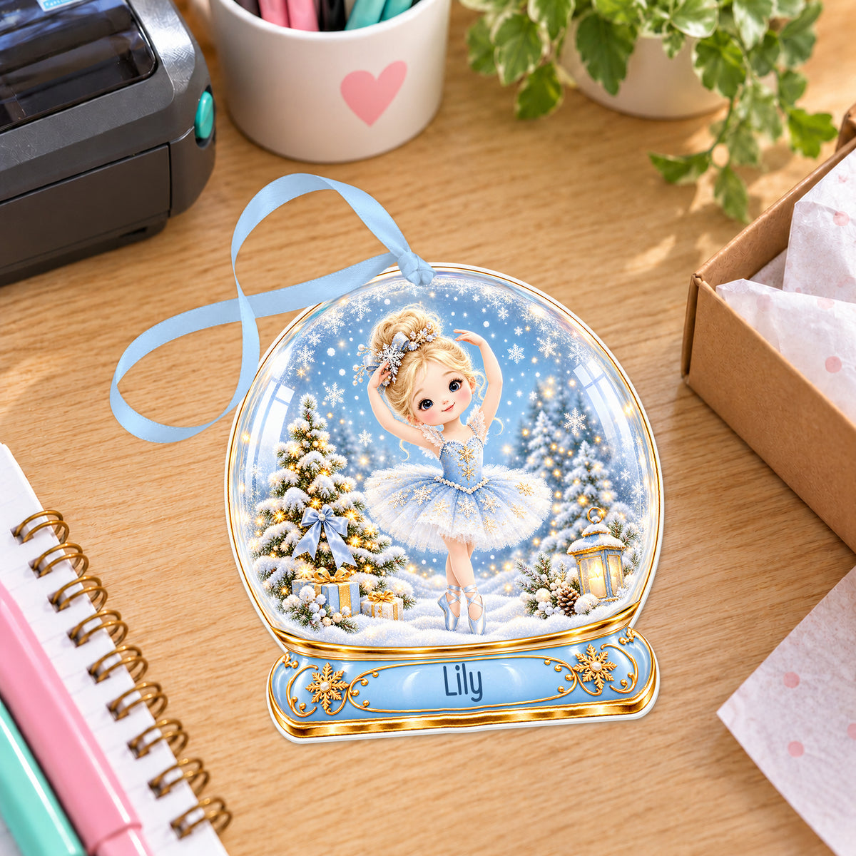 Personalised blue ballerina snow globe bauble with name, white acrylic Christmas decoration with ribbon, shown on a desk